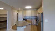 This single-floor residence offers a thoughtfully designed layout with a clean, modern aesthetic throughout. The kitchen serves as a central highlight, featuring light wood cabinetry that extends to the ceiling for ample storage, paired with granite-style countertops that add a touch of elegance. A peninsula island provides additional workspace and a natural gathering point, making the kitchen both practical and inviting. Stainless steel appliances, including a full-size refrigerator and dishwasher, complete the contemporary look. A double-basin sink is positioned beneath upper cabinetry along the back wall, keeping the workspace organized and efficient. The kitchen flows seamlessly into the adjacent living areas, supported by warm light hardwood flooring that runs throughout the main spaces, lending a sense of continuity and warmth. Recessed and flush-mounted ceiling lighting provides consistent illumination across the space. Two interior doors visible from the kitchen suggest convenient access to additional rooms or storage closets, reinforcing the functional layout. Neutral wall tones and clean crown molding contribute to a polished, cohesive interior that is both welcoming and practical.