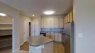 This single-floor residence offers a thoughtfully designed layout with a clean, modern aesthetic throughout. The kitchen serves as a central highlight, featuring light wood cabinetry that extends to the ceiling for ample storage, paired with granite-style countertops that add a touch of elegance. A peninsula island provides additional workspace and a natural gathering point, making the kitchen both practical and inviting. Stainless steel appliances, including a full-size refrigerator and dishwasher, complete the contemporary look. A double-basin sink is positioned beneath upper cabinetry along the back wall, keeping the workspace organized and efficient. The kitchen flows seamlessly into the adjacent living areas, supported by warm light hardwood flooring that runs throughout the main spaces, lending a sense of continuity and warmth. Recessed and flush-mounted ceiling lighting provides consistent illumination across the space. Two interior doors visible from the kitchen suggest convenient access to additional rooms or storage closets, reinforcing the functional layout. Neutral wall tones and clean crown molding contribute to a polished, cohesive interior that is both welcoming and practical.
