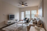 This single-floor residence offers a thoughtfully designed layout that balances comfort and functionality across its key living spaces. The living room serves as the central gathering area, featuring dark hardwood-style flooring, a ceiling fan with light fixture, and large windows flanking a glass-panel exterior door that floods the space with natural light and provides outdoor access. Neutral warm walls throughout create a cohesive, inviting ambiance.

The kitchen is equipped with stainless steel appliances, including a refrigerator, range, and over-the-range microwave. Dark espresso cabinetry pairs with granite countertops, and a peninsula with additional counter space connects to a dedicated dining area with light wood-style flooring — ideal for everyday meals.

The primary bedroom features carpet flooring, a prominent window with slatted blinds offering natural light and outdoor views, and a ceiling fan. A second bedroom is similarly carpeted, bright with dual windows, and versatile in its use.

The bathroom is finished with granite countertops, a dual-sink dark wood vanity, light wood-style tile flooring, and a tiled shower-tub combination with dark geometric wall tile, lending a clean, contemporary feel to the space.