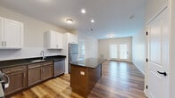 This single-floor, 3-bedroom, 2-bathroom residence offers a well-designed layout that balances functionality and modern style. The open-concept kitchen and living area serves as the heart of the home, where rich hardwood-style flooring flows throughout. The kitchen is outfitted with a two-toned cabinetry design — white upper cabinets paired with warm brown lower cabinets — complemented by dark granite countertops, a subway tile backsplash, and a full suite of stainless steel appliances including a refrigerator, dishwasher, range, and over-the-range microwave. A central kitchen island provides additional prep and seating space. The adjoining living area is bright and airy, featuring neutral walls and a set of French doors that invite natural light and provide outdoor access. The three bedrooms are carpeted and feature neutral tones, with windows offering outdoor views. The spacious primary bedroom offers a comfortable and private retreat. The two bathrooms are finished with tile flooring, warm wood vanities, dark granite countertops, and large mirrors. One bathroom includes a full tub-shower combo with chrome fixtures. A dedicated closet rounds out the practical storage offerings of this thoughtfully appointed residence.