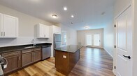 This single-floor, 3-bedroom, 2-bathroom residence offers a well-designed layout that balances functionality and modern style. The open-concept kitchen and living area serves as the heart of the home, where rich hardwood-style flooring flows throughout. The kitchen is outfitted with a two-toned cabinetry design — white upper cabinets paired with warm brown lower cabinets — complemented by dark granite countertops, a subway tile backsplash, and a full suite of stainless steel appliances including a refrigerator, dishwasher, range, and over-the-range microwave. A central kitchen island provides additional prep and seating space. The adjoining living area is bright and airy, featuring neutral walls and a set of French doors that invite natural light and provide outdoor access. The three bedrooms are carpeted and feature neutral tones, with windows offering outdoor views. The spacious primary bedroom offers a comfortable and private retreat. The two bathrooms are finished with tile flooring, warm wood vanities, dark granite countertops, and large mirrors. One bathroom includes a full tub-shower combo with chrome fixtures. A dedicated closet rounds out the practical storage offerings of this thoughtfully appointed residence.
