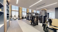 Located at 1556 Northwest 110th Avenue in Miami, FL, this expansive fitness center — branded "Evolve" — delivers a premium exercise experience across a generously sized, single-floor layout. The facility is defined by soaring ceilings and dramatic floor-to-ceiling windows that flood the space with natural light and offer open views of the surrounding Miami skyline and greenery, creating an energizing atmosphere throughout.

The exercise room is organized into distinct functional zones, accommodating a wide spectrum of training modalities. A dedicated cardio section lines the windowed perimeter with a full row of treadmills, ellipticals, stair climbers, and stationary bikes. Strength training is well represented with multiple cable and multi-station machines, power racks, a comprehensive dumbbell rack, kettlebell storage, and medicine balls. Free weight benches and specialty strength equipment, including a leg press, are thoughtfully distributed throughout the open floor plan.

The interior design strikes a balance between high performance and refined aesthetics. Durable rubberized flooring, large wall mirrors, and linear LED lighting fixtures contribute to a clean, modern look. Decorative pendant lighting adds a warm, boutique feel, while large-scale athletic wall murals and a living green wall with the illuminated "Evolve" signage serve as standout design elements. Built-in shelving and glass-partitioned areas further elevate the facility's polished, contemporary character.