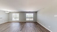 Located at 382 Vinings Dr in Bloomingdale, IL, this single-floor residence offers a thoughtfully designed layout with a clean, contemporary aesthetic throughout. The main living area is generously proportioned, featuring dark hardwood-style flooring and soft gray-toned walls that create a neutral, versatile backdrop. Multiple large windows line the exterior walls, flooding the space with natural light and providing views of the surrounding greenery. A sliding glass door or oversized window panel opens the living area toward what appears to be an outdoor deck or balcony, enhancing the connection between interior and exterior spaces.

The open-concept layout connects the living area to a dining space and kitchen. The kitchen is well-appointed with white cabinetry, granite-style countertops, a subway tile backsplash, and stainless steel appliances including a refrigerator, range, and microwave. Hardwood-style flooring continues seamlessly through these areas.

The bedroom features plush carpeting and soft neutral walls, offering a quieter, more comfortable atmosphere. The bathroom is finished with white tile in the tub/shower surround, a white vanity with chrome fixtures, and matching hardwood-style flooring, maintaining a cohesive design language throughout the home.
