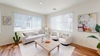 This single-story residence offers a thoughtfully designed layout encompassing two bedrooms, two bathrooms, an office, a living room, and a kitchen — all connected by a functional hallway. The open-concept kitchen is a standout feature, showcasing warm honey-toned wood cabinetry, granite countertops, a central island with seating, track lighting, and wood-look flooring that extends throughout the main living areas. White appliances including a refrigerator, dishwasher, range, and microwave complete the space, while large windows allow generous natural light to fill the room.

The living room continues the bright, airy aesthetic with multiple oversized windows dressed in vertical blinds, creating an inviting and well-lit gathering area. The primary bedroom offers a comfortable, carpeted retreat with a walk-in closet and a dedicated en-suite bathroom featuring a walk-in shower with built-in shelving. The second bedroom is equally well-lit, with a large window and soft carpet underfoot. The second bathroom includes a full tub-shower combination, wood-look flooring, and a granite-topped vanity. The additional office provides flexible space for work or other needs. Throughout, the neutral color palette and clean finishes contribute to a cohesive, welcoming ambiance.