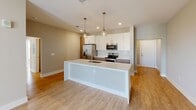Located at 222 S Main St in Mooresville, NC, this well-appointed 2-bedroom, 2-bathroom residence offers a thoughtfully designed single-level layout with modern finishes throughout. The open-concept kitchen and living area serves as the heart of the home, anchored by a large central island with a white quartz countertop, undermount sink, and striking pendant lighting. White shaker-style upper cabinets are paired with warm wood-toned lower cabinets, complemented by stainless steel appliances including a French door refrigerator, electric range, and built-in microwave. Light wood-look flooring flows seamlessly throughout the entire residence, creating a bright and cohesive aesthetic. The spacious primary bedroom features multiple windows that invite abundant natural light, a ceiling fan, and direct access to a generous walk-in closet outfitted with wire shelving systems. The primary bathroom includes a dual-sink vanity with quartz countertops, wood-toned cabinetry, and framed mirrors. The second bedroom offers built-in wall shelving, dual windows with outdoor views, and a private exterior door. Neutral warm-toned walls and clean white trim unify the space, contributing to an airy, contemporary ambiance throughout.