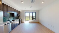 This well-designed single-floor unit offers a seamless blend of contemporary style and functional living. The open-concept living and kitchen area is anchored by light hardwood-style flooring and recessed lighting throughout, creating a bright and welcoming atmosphere. Large sliding glass doors lead to a private balcony, flooding the living space with natural light and offering pleasant views of the surrounding landscape.

The kitchen is a standout feature, showcasing rich dark-stained wood cabinetry extending from floor to ceiling, paired with crisp white countertops and a striking teal subway tile backsplash. A full suite of stainless steel appliances — including a side-by-side refrigerator with ice maker, dishwasher, microwave, and range — provides everything needed for everyday cooking and entertaining.

The bedroom is a calm, neutral retreat with the same warm hardwood-style flooring, recessed lighting, and clean white walls, offering a versatile and peaceful space. The bathroom is finished with dark floor tiles, a dark wood vanity topped with a white countertop, matte black hardware accents, and a glass-enclosed walk-in shower with white subway tile, delivering a clean, modern aesthetic throughout.