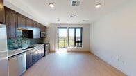 This well-designed single-floor unit offers a seamless blend of contemporary style and functional living. The open-concept living and kitchen area is anchored by light hardwood-style flooring and recessed lighting throughout, creating a bright and welcoming atmosphere. Large sliding glass doors lead to a private balcony, flooding the living space with natural light and offering pleasant views of the surrounding landscape.

The kitchen is a standout feature, showcasing rich dark-stained wood cabinetry extending from floor to ceiling, paired with crisp white countertops and a striking teal subway tile backsplash. A full suite of stainless steel appliances — including a side-by-side refrigerator with ice maker, dishwasher, microwave, and range — provides everything needed for everyday cooking and entertaining.

The bedroom is a calm, neutral retreat with the same warm hardwood-style flooring, recessed lighting, and clean white walls, offering a versatile and peaceful space. The bathroom is finished with dark floor tiles, a dark wood vanity topped with a white countertop, matte black hardware accents, and a glass-enclosed walk-in shower with white subway tile, delivering a clean, modern aesthetic throughout.