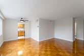 This single-floor unit is defined by its striking polished parquet wood flooring, laid in a classic checkerboard pattern that extends throughout the living areas and bedrooms, adding warmth and visual interest underfoot.

The open living area is generously proportioned, with neutral-toned walls, clean white ceilings, and a ceiling fan providing overhead circulation. The space connects seamlessly to the kitchen, which features warm honey-toned wood cabinetry extending to the upper walls, offering considerable storage. The kitchen is equipped with black appliances, including a gas range, dishwasher, and refrigerator, alongside a double-basin sink and speckled laminate countertops. Light ceramic tile flooring completes this functional space.

Two bedrooms are present, each continuing the parquet flooring and offering closet storage, including mirrored sliding-door closets. Large windows dressed with vertical blinds allow generous natural light and views of surrounding greenery.

Two bathrooms serve the unit. The full bathroom features light tile flooring, a shower-tub combination, a vanity with a single sink, and a mirror. The half bathroom includes a vanity, mirror, and toilet in a compact, practical layout.