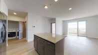 Located at 6518 Milwaukee St in Madison, WI, this modern single-floor residence offers a thoughtfully designed open-concept layout with clean lines and contemporary finishes throughout. The kitchen serves as a central highlight, featuring gray shaker-style cabinetry, granite countertops, a large center island with additional granite surface space, and a full suite of stainless steel appliances including a refrigerator with ice maker, dishwasher, and range. Recessed lighting and tile flooring complete the kitchen's polished look. The kitchen flows seamlessly into a spacious living area finished with light hardwood flooring and large sliding glass doors that open to a private balcony, flooding the space with natural light and offering open views of the surrounding Madison landscape. The bedroom is generously sized, featuring the same light hardwood flooring, a ceiling fan, and a large window that captures abundant natural light and scenic outdoor views. The bathroom is well-appointed with large-format tile flooring, a stylish blue vanity with white quartz countertop, and modern hardware. A dedicated laundry area is also present within the unit. Throughout the residence, white walls, modern door finishes, and consistent flooring choices create a cohesive, contemporary aesthetic.