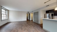 This single-floor residence at 1211 Euclid Ave in Cleveland, Ohio, offers a well-designed layout with a cohesive blend of modern finishes and functional spaces. The open living area is finished with rich wood-look flooring and neutral-toned walls, creating a versatile and welcoming environment. Multiple large windows allow generous natural light to fill the space, offering views of the surrounding urban streetscape.

The kitchen is a standout feature, outfitted with dark espresso cabinetry, quartz countertops, a classic white subway tile backsplash, and stainless steel appliances including an electric range and over-the-range microwave. Pendant lighting and a breakfast bar peninsula connect the kitchen to the living area, enhancing the open-concept flow.

The bedroom is carpeted for comfort and receives natural light through a sizable window. Storage is provided by a double-door closet visible from the main living space.

Two bathrooms serve the unit. One features dark cabinetry, a white countertop vanity, a large mirror, and wood-look flooring, while the second is more utilitarian, with light tile flooring, a dark vanity, and a towel bar. Both maintain the consistent neutral palette found throughout the residence.