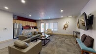 Located at 4101 Monona Dr in Monona, Wisconsin, this single-floor community space is thoughtfully designed to encourage comfort and gathering. The main lounge area is generously sized, featuring patterned carpet flooring and recessed lighting that creates a warm, inviting atmosphere throughout. Plush leather sofas and upholstered armchairs are arranged around a sleek coffee table, offering ample seating for socializing or relaxing. Natural light filters in through multiple windows fitted with blinds, adding brightness to the space.

A built-in kitchenette lines one wall of the lounge, finished with light maple cabinetry, granite-style countertops, a double-basin stainless steel sink, and room for small appliances such as a coffee maker and microwave. A full-size stainless steel refrigerator completes the functional setup. A bold deep-red accent wall adds a striking visual contrast to the neutral tones throughout the space.

Decorative wall art, including sculptural pieces, adds character and a creative touch to the lounge. A wall-mounted flat-screen television and bench seating provide an additional media area. Adjacent to the main lounge is a private meeting room featuring a large table and metal chairs, accented by the same rich red wall color and framed artwork, making it suitable for small group discussions or meetings.