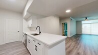 This well-appointed single-floor home offers three bedrooms and two bathrooms within a thoughtfully designed layout. The open-concept kitchen and living area serves as the heart of the home, featuring a large central island with a striking white quartz countertop, undermount sink, and matte black fixtures. White shaker cabinetry, stainless steel appliances, and recessed lighting complete the kitchen's clean, modern aesthetic. Wood-look luxury vinyl plank flooring flows seamlessly throughout the entire home, tying the spaces together cohesively. A wide hallway connects the bedrooms, each of which is bright and well-proportioned, with large windows dressed in roller shades that allow for ample natural light. The spacious primary bedroom includes a ceiling fan and generous proportions. Both bathrooms are finished with neutral large-format tile surrounds and white quartz vanity tops. The primary bath stands out with a separate glass-enclosed walk-in shower alongside a soaking tub, while the secondary bath features a tub-shower combination. Crown molding and white panel doors add refined detail throughout, giving the entire home a polished, move-in-ready feel.