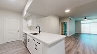 This well-appointed single-floor home offers three bedrooms and two bathrooms within a thoughtfully designed layout. The open-concept kitchen and living area serves as the heart of the home, featuring a large central island with a striking white quartz countertop, undermount sink, and matte black fixtures. White shaker cabinetry, stainless steel appliances, and recessed lighting complete the kitchen's clean, modern aesthetic. Wood-look luxury vinyl plank flooring flows seamlessly throughout the entire home, tying the spaces together cohesively. A wide hallway connects the bedrooms, each of which is bright and well-proportioned, with large windows dressed in roller shades that allow for ample natural light. The spacious primary bedroom includes a ceiling fan and generous proportions. Both bathrooms are finished with neutral large-format tile surrounds and white quartz vanity tops. The primary bath stands out with a separate glass-enclosed walk-in shower alongside a soaking tub, while the secondary bath features a tub-shower combination. Crown molding and white panel doors add refined detail throughout, giving the entire home a polished, move-in-ready feel.