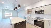This modern 1-bedroom, 2-bathroom unit at 352 S 500 E in Salt Lake City's vibrant East Side neighborhood offers a well-designed open-concept layout across a single floor. Light hardwood flooring flows seamlessly throughout, creating a clean and cohesive aesthetic.

The combined kitchen and living area serves as the heart of the unit. The kitchen is outfitted with sleek white flat-panel cabinetry, open wood shelving, a herringbone-pattern tile backsplash, and a full suite of stainless steel appliances including a range, dishwasher, microwave, and refrigerator. A two-tone island with a white countertop and dark base, accented by pendant lighting, provides additional prep space and casual seating. The living area extends naturally from the kitchen, bathed in natural light from large windows with views of the surrounding cityscape and greenery.

The bedroom is a comfortable, private retreat with a large window, light-toned walls, and access to a walk-in closet with dual hanging rods and shelving. Both bathrooms are finished in a clean, minimalist style, with one featuring a sliding glass-enclosed walk-in shower. Throughout the unit, recessed lighting, white walls, and light wood floors contribute to a bright, contemporary ambiance ideal for modern urban living.