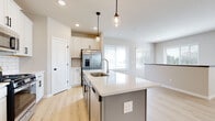 This thoughtfully designed two-story home offers a clean, contemporary aesthetic throughout. The heart of the main level is a stylish kitchen featuring white shaker cabinetry, subway tile backsplash, a light blue center island with a white quartz countertop, an integrated sink, and pendant lighting. Stainless steel appliances — including a French door refrigerator, gas range, and microwave — complete the space. Light hardwood flooring flows through the main living areas, while large windows fitted with horizontal blinds fill the rooms with natural light and create an open, airy atmosphere. The open living area offers a welcoming layout with recessed lighting and neutral tones throughout. Bedrooms are carpeted for comfort, including a spacious room with generous natural light. A primary bathroom presents a dual-sink vanity with white quartz counters, white cabinetry with matte black hardware, and a full tub-shower combination. A sizable walk-in closet with wire shelving provides ample storage. A dedicated laundry room houses a full-size top-load washer and dryer with additional shelving above. The lower level features an unfinished basement with concrete walls and flooring, offering substantial potential for customization or additional storage.