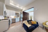This thoughtfully designed single-floor residence combines modern aesthetics with functional living. The open-concept layout seamlessly connects the living area to the kitchen, creating a bright and cohesive space. A distinctive slatted wood divider adds architectural character while subtly defining the living zone, which benefits from a large floor-to-ceiling window that floods the space with natural light and provides access to a balcony.

The kitchen is well-equipped with white shaker-style cabinetry, crisp white countertops, a marble-style tile backsplash, and a full suite of stainless steel appliances including a gas range, over-the-range microwave, dishwasher, and a French door refrigerator. Open shelving provides both storage and display opportunities, and durable hardwood-style flooring runs throughout the main living and kitchen areas.

The bedroom is a calm, restful retreat finished in warm neutral tones with plush carpeting and a double-door closet offering generous storage. A hallway connects the bedroom to a full bathroom, which features a combination tub and shower, tiled flooring, a wood-toned vanity with a white countertop, and clean shiplap-style wall tiling. A louvered closet door in the hallway conceals a convenient in-unit laundry area, completing this well-rounded and efficiently planned residence.