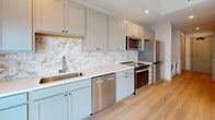 Located at 304 E Jackson Blvd in Elkhart, Indiana, this thoughtfully designed studio unit offers a clean, modern aesthetic across a single floor. Light hardwood flooring flows throughout, tying together the open-concept living, dining, and kitchen area, which is anchored by large windows that invite natural light and provide views of the surrounding cityscape.

The kitchen is a standout feature, showcasing gray shaker-style cabinetry, white quartz countertops, and a striking marble-look tile backsplash. A full suite of stainless steel appliances — including a refrigerator, range, microwave, and dishwasher — ensures both function and style. An in-unit washer is conveniently tucked near the kitchen entry corridor.

The living area is bright and open, with a ceiling fan and recessed lighting providing comfort and ambiance. Roller shades on the oversized windows offer privacy while maintaining the airy feel of the space.

The bathroom features light hardwood-style flooring, a walk-in shower, a toilet, and a vanity with ample cabinetry and a white countertop. Two closets provide generous storage throughout the unit.

Neutral wall tones and modern finishes give this unit a fresh, move-in-ready feel well-suited for efficient urban living.
