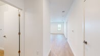 This thoughtfully designed single-floor unit offers a clean, modern aesthetic throughout, characterized by crisp white walls, light wood-tone luxury vinyl flooring, and an abundance of natural light from multiple windows with blinds. The open-concept living and dining area provides a welcoming, airy atmosphere, anchored by a front entry door and seamless flow into the kitchen. The kitchen is well-appointed with warm wood-grain flat-panel cabinetry accented by matte black hardware, white quartz countertops, a stainless steel undermount sink, and a full suite of stainless steel appliances including a range, over-the-range microwave, and dishwasher. Light wood flooring runs through the main living areas, creating a cohesive, contemporary feel. The bedrooms are finished with plush neutral carpeting, ceiling fans, and windows that bring in natural views and daylight. The bathrooms feature warm wood-tone vanity cabinetry with white countertops, large framed mirrors, and tile-surround walk-in glass enclosed showers. A hallway with wood-look flooring connects the living areas to the private rooms, contributing to the home's efficient and functional layout. Overall, the unit presents a fresh, move-in-ready environment with modern finishes throughout.