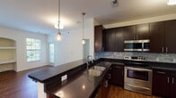 Located at 5453 Clemwood Ct SE in Ada, Michigan, this single-floor residence offers a well-designed layout with a clean, contemporary aesthetic throughout. The kitchen is a standout feature, showcasing rich dark espresso cabinetry, dark granite countertops, a textured tile backsplash, and stainless steel appliances including a range and over-the-range microwave. A peninsula with a double undermount sink and pendant lighting connects the kitchen to the open living and dining area, which is finished with warm hardwood-style flooring. The living area is generously sized, bathed in natural light from multiple windows, and includes a charming built-in arched shelving unit and dedicated desk nook. The bedrooms are carpeted and well-lit, with windows offering views of the surrounding neighborhood. A ceiling fan adds comfort to the primary bedroom. Two full bathrooms each feature a tub-shower combination, dark vanity cabinetry, and hardwood-style flooring, with one bathroom including a large vanity mirror. The overall ambiance of the space is bright, clean, and move-in ready, combining practical functionality with modern finishes throughout.
