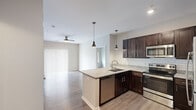 This three-bedroom, two-bathroom single-floor residence in Coralville, Iowa offers a well-designed layout with modern finishes throughout. The open-concept kitchen and dining area serves as the heart of the home, showcasing rich dark-wood cabinetry, granite countertops, a classic white subway tile backsplash, and a full suite of stainless steel appliances including a refrigerator, electric range, and built-in microwave. Stylish pendant lighting illuminates the peninsula, which provides additional prep space and a natural gathering point that flows into the living area. Hardwood-style flooring runs consistently throughout the main living spaces, complementing the neutral, warm-toned walls and creating a cohesive aesthetic. The living area is bright and airy, featuring a ceiling fan and a sliding glass door dressed with vertical blinds that invites natural light. The primary bedroom is a comfortable retreat with its own ceiling fan, direct access to a private bathroom with a walk-in shower, and a dedicated walk-in closet. The second bathroom features a full tub-shower combination with brushed nickel fixtures and grab bars. Additional closets provide ample storage, while a hallway connects the bedrooms efficiently. The overall ambiance is clean, contemporary, and move-in ready.
