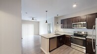 This three-bedroom, two-bathroom single-floor residence in Coralville, Iowa offers a well-designed layout with modern finishes throughout. The open-concept kitchen and dining area serves as the heart of the home, showcasing rich dark-wood cabinetry, granite countertops, a classic white subway tile backsplash, and a full suite of stainless steel appliances including a refrigerator, electric range, and built-in microwave. Stylish pendant lighting illuminates the peninsula, which provides additional prep space and a natural gathering point that flows into the living area. Hardwood-style flooring runs consistently throughout the main living spaces, complementing the neutral, warm-toned walls and creating a cohesive aesthetic. The living area is bright and airy, featuring a ceiling fan and a sliding glass door dressed with vertical blinds that invites natural light. The primary bedroom is a comfortable retreat with its own ceiling fan, direct access to a private bathroom with a walk-in shower, and a dedicated walk-in closet. The second bathroom features a full tub-shower combination with brushed nickel fixtures and grab bars. Additional closets provide ample storage, while a hallway connects the bedrooms efficiently. The overall ambiance is clean, contemporary, and move-in ready.