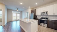 This single-floor residence showcases a thoughtfully designed open-concept layout where the kitchen seamlessly connects to the living area. The kitchen is a standout feature, centered around a large island with a granite countertop and integrated sink, offering ample workspace and casual seating potential. Cabinetry combines crisp white upper cabinets with rich dark espresso lower cabinets, accented by a neutral tile backsplash. Stainless steel appliances, including a refrigerator, range, and microwave, complete the modern aesthetic. Wood-look flooring runs throughout the main living areas, adding warmth and continuity.

The bedrooms feature plush carpeting and generous natural light through large windows with horizontal blinds, offering pleasant outdoor views. Ceiling fans are present in multiple rooms. The bathrooms are well-finished, featuring dark navy cabinetry topped with granite countertops, undermount sinks, large mirrors, and wood-look tile flooring. The primary bathroom includes a spacious glass-enclosed walk-in shower with marble-style tile surround. Recessed lighting throughout the unit provides consistent, functional illumination across all spaces.