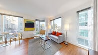 Located at 1188 Mission Street in San Francisco's vibrant SoMa neighborhood, Unit 302 is a thoughtfully designed residence that combines modern aesthetics with functional living. The unit features warm hardwood flooring throughout, crisp white walls, and an abundance of natural light streaming through large floor-to-ceiling windows.

The living room is an inviting, light-filled space anchored by oversized windows offering urban views of the surrounding cityscape. The open layout comfortably accommodates a seating area and provides a welcoming atmosphere ideal for relaxing or entertaining.

The kitchen is efficiently laid out with clean white cabinetry extending to the ceiling, a full-size refrigerator, a range, and ample counter space. A dining area positioned beside a large window completes this functional space.

The primary bedroom is generously sized, bathed in natural light from dual windows overlooking neighboring buildings and greenery, with warm hardwood floors adding to the serene ambiance. A second bedroom offers a built-in closet and additional sleeping quarters. The full bathroom is finished in clean white tile, featuring a soaking tub with shower, built-in shelving, and a vanity with dark countertops and a large mirror.