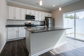 Located at 6412 Shallowford Rd in Chattanooga, Tennessee, this single-story home offers a clean, modern aesthetic with consistent dark hardwood-style flooring and crown molding throughout. The open-concept layout seamlessly connects the living area and kitchen, creating a spacious and functional flow. The living room is bright and airy, benefiting from natural light streaming through windows and a sliding glass door that leads to an outdoor area, complemented by a ceiling fan overhead.

The kitchen is well-appointed with white shaker-style cabinetry, granite countertops, a subway tile backsplash, and a full suite of stainless steel appliances including a range, over-the-range microwave, and refrigerator. Pendant lighting accents the kitchen island, which features its own granite surface and undermount sink, adding both style and utility.

The bedrooms are comfortably sized with ceiling fans, natural window light, and generous closet space, including a walk-in closet outfitted with wire shelving. The bathroom continues the home's cohesive design with white cabinetry, granite countertops, and an undermount sink. Throughout, the neutral color palette and quality finishes create a welcoming and well-maintained living environment.