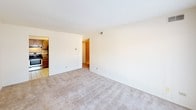 This single-floor residential unit offers a practical and comfortable layout across several well-defined spaces. The living area is generously sized, featuring neutral-toned wall-to-wall carpeting and crisp white walls that create a clean, open feel. A large sliding glass door fitted with vertical blinds floods the room with natural light and provides access to an outdoor area. An adjacent room, also carpeted and finished in the same neutral palette, offers versatility as a bedroom or secondary living space, with a window overlooking the exterior.

The kitchen is a functional highlight of the unit, outfitted with rich warm-toned wood cabinetry, granite-look countertops, and white tile flooring. Stainless steel appliances include a gas range with oven, a dishwasher, and a refrigerator, complemented by an under-cabinet range hood and a double-basin stainless steel sink. Ample upper and lower cabinet storage maximizes the utility of the space.

The bathroom is neatly appointed with white tile flooring, a full tub-and-shower combination with tiled surround, a toilet, and a vanity with a wood cabinet base, white countertop, and a mirrored medicine cabinet above. The overall design throughout the unit is clean, understated, and move-in ready.