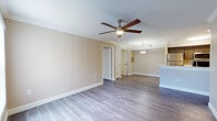 This single-floor residence features a cohesive, modern design highlighted by wood-style plank flooring that runs throughout the living areas and bedrooms, providing a warm, unified aesthetic. The open-concept living and dining area is generously proportioned, finished with neutral beige walls, crown molding accents, and a ceiling fan with integrated lighting. A pendant light fixture illuminates the transition between the living space and the kitchen, which features a peninsula with a built-in sink, dark cabinetry, white countertops, and stainless steel appliances including a refrigerator, electric range, and microwave.

Multiple bedrooms share a consistent design language — each equipped with a ceiling fan, neutral walls, wood-style flooring, and a window fitted with vertical blinds that allows natural light to enter. The bathrooms are finished with tile flooring, white tiled tub and shower combinations with chrome fixtures, and vanities featuring dark cabinetry paired with light countertops. The overall ambiance throughout is clean, neutral, and functional, offering a move-in-ready environment with a cohesive design palette.