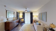 This single-floor residence offers a thoughtfully designed layout that balances comfort and functionality across its key living spaces. The living room serves as the heart of the home, featuring wood-style flooring, a ceiling fan, and a large sliding glass door fitted with vertical blinds and dark curtain panels, allowing for flexible light control. The space comfortably accommodates a full seating arrangement, complemented by warm ambient lighting.

The galley-style kitchen is outfitted with white cabinetry, granite-look countertops, a tile backsplash, and stainless steel appliances, including a refrigerator, range, and microwave. Wood-style flooring continues throughout, and ample counter space supports everyday meal preparation.

A dedicated dining area adjacent to the main living space features a round glass-top table beneath a pendant light fixture, creating a defined yet intimate setting for meals.

The bedroom is generously sized with its own ceiling fan, wood-style flooring, and a window that draws in natural light. It connects to a well-finished bathroom featuring granite-look countertops, an undermount sink, and gray cabinetry with brushed nickel hardware. Consistent neutral tones throughout the residence create a cohesive and inviting atmosphere.