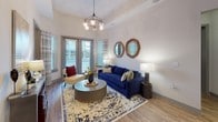 This single-story residence offers a thoughtfully designed open-concept floor plan with notable architectural details, including soaring vaulted ceilings that lend a sense of spaciousness throughout the living areas. The living room serves as a central gathering space, featuring hardwood-style flooring, large glass doors that open to a private balcony, and abundant natural light. An elegant chandelier adds a refined focal point overhead.

The kitchen is well-equipped with rich dark-stained cabinetry extending to the ceiling, stainless steel appliances including a refrigerator, range, microwave, and dishwasher, complemented by granite countertops, a glass tile backsplash, and under-cabinet lighting. A generous island provides additional workspace and casual seating.

The primary bedroom features vaulted ceilings, plush carpeting, and access to natural light, while a secondary bedroom includes a walk-in closet for ample storage. Each bathroom is distinctly finished: one offers a glass-enclosed walk-in shower with floor-to-ceiling grey tile, while the other features a full soaking tub with subway tile surround. Both bathrooms include dark vanity cabinetry and granite countertops, delivering a cohesive, modern aesthetic throughout.