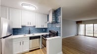 Located at 392 State St in North Haven, Connecticut, this thoughtfully renovated single-floor residence offers a clean, modern aesthetic throughout. The open living area is finished with warm hardwood flooring, soft gray walls, and crisp white baseboards, creating a bright and welcoming atmosphere. A large sliding glass door floods the space with natural light and provides access to an outdoor balcony with views of the surrounding greenery.

The kitchen is a standout feature, showcasing white shaker cabinetry with matte black hardware, light quartz countertops, and a striking blue subway tile backsplash that adds a bold design element. Stainless steel appliances — including a refrigerator, electric range, dishwasher, and a wall-mounted range hood — complete this functional and stylish space.

The bathroom continues the blue tile theme, with glossy navy subway tile lining the tub surround from floor to ceiling, paired with a white vanity and matte black fixtures for a cohesive, contemporary look.

The bedrooms are carpeted for comfort and include windows that invite natural light, along with baseboard heating. Additional rooms feature neutral finishes, offering flexible use of space. Throughout, the unit maintains a clean, move-in-ready condition with consistent modern updates.