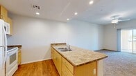 Located in Hesperia, CA, this single-story 2-bedroom, 2-bathroom home offers a practical and well-organized layout. The open-concept kitchen and dining area serves as the heart of the home, featuring light wood cabinetry, stone-look countertops, a double stainless steel sink, and white appliances including a refrigerator, range, and microwave. Recessed lighting illuminates the space, which is finished with warm wood-look vinyl flooring that extends throughout the kitchen and common areas. A peninsula counter creates a natural divide between the kitchen and the adjoining living and dining spaces. Both bedrooms are comfortably sized, with the primary bedroom offering generous proportions, soft wall-to-wall carpeting, and windows that bring in natural light and views of the surrounding area. The second bedroom mirrors this design with carpeted floors and ample natural light. Each bathroom is well-appointed with matching wood-tone vanities, stone-look countertops, and wood-look flooring. The primary bathroom features a glass-enclosed walk-in shower with white tile surround. Additional highlights include a dedicated laundry area, a closet for storage, a hallway connecting the rooms efficiently, and a balcony for outdoor enjoyment.