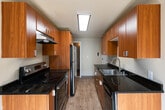 This single-floor residence offers a well-organized layout that balances comfort and functionality. The galley-style kitchen is a standout feature, boasting warm wood cabinetry, dark granite countertops, stainless steel appliances including a refrigerator, electric range, and dishwasher, and light hardwood-style flooring — all illuminated by a skylight panel overhead. A hallway connects the main living areas, with a closet providing convenient storage access near the entry.

The living area is generously proportioned, featuring plush wall-to-wall carpeting and a large picture window that frames views of the surrounding urban streetscape, allowing abundant natural light to fill the room. Baseboard heating runs along the perimeter of the windowed rooms, ensuring year-round comfort. The bedroom similarly offers carpeted flooring and a sizable window with city views, creating a bright and airy atmosphere.

The bathroom features a full-size soaking tub with an overhead shower, accented by gray surround walls and chrome fixtures, alongside a white sink vanity with mirror. Throughout the residence, neutral wall tones and clean white trim contribute to a cohesive, understated aesthetic well-suited for urban living.