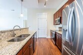 This single-floor residence offers a thoughtfully designed open-concept layout that seamlessly connects the living area and kitchen. Rich hardwood flooring flows throughout the main living spaces, complemented by neutral walls that create a bright, welcoming atmosphere. The spacious living area is bathed in natural light from large windows and French doors, and is finished with a ceiling fan for added comfort. A generous kitchen anchors the space with deep-toned wood cabinetry, light granite countertops, a decorative tile backsplash, and a full suite of stainless steel appliances including a refrigerator, range, and built-in microwave. A peninsula with pendant lighting provides additional workspace and serves as a natural divider between the kitchen and living areas. The bedrooms feature plush carpeting, ceiling fans, and windows that bring in ample natural light. Two bathrooms are finished consistently with granite-topped vanities, rich wood cabinetry, and hardwood-style flooring — one with a tub-shower combination and one with a walk-in shower, both equipped with grab bars. Throughout the residence, the cohesive design elements and quality finishes create a clean, functional, and comfortable living environment.