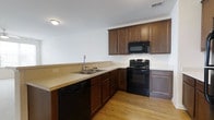 Located at 36916 Crooked Hammock Way in Lewes, Delaware, this single-floor home offers a practical and well-appointed layout designed for comfortable living. The kitchen is a standout feature, showcasing rich dark wood cabinetry that provides ample storage space along the upper and lower walls. A full suite of black appliances — including a gas range, built-in microwave, and dishwasher — complements the cabinetry for a cohesive, classic look. The countertops are finished in a neutral tone, offering generous workspace, while the double-basin sink with a modern faucet is conveniently positioned along the peninsula-style counter. Warm, light-toned hardwood-style flooring runs throughout the kitchen, adding brightness and continuity to the space. Recessed and flush-mount ceiling lighting ensures the kitchen is well-lit. The overall design reflects a functional, low-maintenance aesthetic suited for everyday use. Situated in the welcoming community of Lewes, DE, this home benefits from its location in a charming coastal region known for its relaxed lifestyle and natural surroundings.
