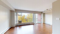 This single-floor residence offers a well-organized layout that balances comfort and functionality. The spacious living area is a standout feature, showcasing warm hardwood flooring that extends throughout the main living spaces. A large picture window and sliding glass door flood the room with natural light and frame beautiful treetop views, with direct access to a private balcony overlooking a lush canopy and city skyline beyond. Track lighting overhead adds a modern accent to the living space.

The galley-style kitchen is efficiently designed with white cabinetry, dark countertops, a stainless steel sink, and full appliances including a refrigerator. Hardwood flooring continues into the kitchen, maintaining a cohesive aesthetic throughout.

The bedroom is carpeted for comfort and features a window with treetop and city views, a baseboard heating unit, and a built-in closet with sliding doors offering shelving and hanging space. The entry area provides a welcoming transition into the unit with clean, neutral-toned walls and hardwood floors.

The bathroom includes a full soaking tub with shower, a pedestal-style vanity with mirrored medicine cabinet storage, and warm-toned flooring. Baseboard heating throughout the unit ensures year-round comfort. The overall ambiance is clean, bright, and functional.