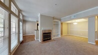 Located at 16650 Huebner Rd in San Antonio, Texas, this single-floor residence offers a thoughtfully designed layout with a warm, neutral color palette throughout. The spacious living area is anchored by a tiled fireplace with a classic white mantle and flanked by a built-in shelving unit with an arched accent, providing both storage and a refined architectural detail. Large, multi-pane windows flood the living space with natural light and offer outdoor views, while plush carpeting adds a comfortable, inviting feel. Crown molding runs throughout the main living and dining areas, contributing to an elegant overall finish. The dining area, visible from the living room, features a decorative pendant light fixture and chair rail detailing. The galley-style kitchen is well-appointed with dark espresso cabinetry, granite countertops, stainless steel appliances including a refrigerator, electric range, and built-in microwave, and warm hardwood-style flooring. Two generously sized bedrooms each include ceiling fans and windows with outdoor views. The bathrooms are finished with dark wood vanities, granite countertops, and large mirrors, with one bathroom featuring a tiled tub-shower combination and wood-style flooring.