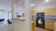 This single-story residence offers a thoughtfully designed layout with cohesive finishes across all rooms. The kitchen is well-equipped, featuring light maple cabinetry extending to the upper walls, granite-style countertops, black appliances including an electric range, built-in microwave, and refrigerator, and durable wood-look flooring. A pass-through counter with a granite top connects the kitchen to the adjacent living area, enhancing the open feel between spaces.

The living room is bright and welcoming, with a ceiling fan, neutral walls, and a large sliding glass door fitted with vertical blinds that open to an outdoor view, allowing generous natural light to fill the space. A seating nook adjacent to the living area also benefits from the sliding door's light and outdoor views.

Both bedrooms are carpeted and feature ceiling fans, large windows with blinds and patterned curtains, and a calm, neutral color palette. The primary bedroom is notably spacious with ample room for a full furniture arrangement.

The bathroom includes a granite-topped vanity with maple cabinetry, wood-look flooring, a tiled shower or soaking tub area, and access to a walk-in closet. Track lighting and recessed fixtures provide consistent illumination throughout the home.