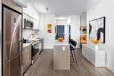Unit 606 at 22 Hughson St is a thoughtfully designed one-bedroom, one-bathroom residence offering a contemporary open-concept layout finished with light hardwood flooring and crisp white walls throughout. The kitchen is a functional centerpiece, equipped with stainless steel appliances including a range, built-in microwave, and dishwasher, complemented by two-tone cabinetry, a subway tile backsplash, light quartz countertops, and a freestanding island with bar seating. The kitchen flows seamlessly into the living and dining areas, creating a cohesive and efficient use of space. The primary living area is bright and airy, featuring floor-to-ceiling windows and a sliding glass door that opens onto a private balcony with urban city views. A secondary living area provides flexible space ideal for a home office or reading nook. The bedroom benefits from large windows framing city views, a mirrored sliding-door closet, and light-filled proportions. The bathroom is well-appointed with a white vanity, soaker tub, and marble-style tile surround. A hallway connects all rooms efficiently, completing this well-planned and modern urban residence.