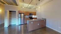 This single-floor loft space masterfully combines industrial heritage with contemporary living. Polished concrete floors run throughout, reflecting light and lending a sleek, cohesive feel to every room. The living area is an immediate showstopper, anchored by an exposed brick accent wall, large arched and rectangular windows that flood the space with natural light, and a wood-planked ceiling with visible beams and exposed ductwork that emphasize the building's historic character. A decorative spiral staircase adds an architectural focal point near the entry.

The kitchen is well-appointed with warm-toned wood cabinetry, granite-look countertops, stainless steel appliances including a refrigerator, electric range with microwave, and dishwasher. A peninsula provides additional prep and seating space, while pendant lighting above adds a refined industrial touch to the room.

The bedroom area offers generous closet space, with original structural columns adding to the authentic loft aesthetic. An original cast-iron pipe column serves as a striking design element. The bathroom includes a full tub/shower combo, a wood-cabinet vanity, and polished nickel fixtures. A dedicated laundry closet houses a full-size side-by-side Whirlpool washer and dryer, completing this well-equipped and character-rich space.