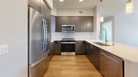 Located at 1774 Metro Avenue in Chula Vista, California, this modern single-floor apartment offers 880 square feet of well-designed living space across 2 bedrooms and 2 bathrooms. The open-concept kitchen and living area serve as the heart of the unit, featuring rich dark cabinetry, a stunning marble-look quartz countertop island, stainless steel appliances including a French door refrigerator, gas range, microwave, and dishwasher, complemented by a white subway tile backsplash and warm wood-look flooring. The living area is bathed in natural light through large sliding glass doors and a transom window that open to an outdoor balcony. Both bedrooms are carpeted and offer a calm, neutral palette; the primary bedroom measures 150 square feet and features a large window with exterior views. Each bedroom is served by its own dedicated closet and hallway access. The two bathrooms are finished with wood-look luxury vinyl flooring, dark vanity cabinetry, white quartz countertops, and large mirrors. One bathroom includes a walk-in shower, while the other offers a tub-shower combo with white subway tile surround. The unit maintains a clean, contemporary aesthetic throughout with neutral warm-gray walls and crisp white trim.