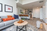 Located in Madison, WI, this modern 3-bedroom, 2-bathroom unit showcases an impressive open-concept design defined by soaring concrete ceilings and dramatic floor-to-ceiling windows that flood the interior with natural light. The combined kitchen and living area serves as the heart of the home, where the living room's expansive glazed walls frame sweeping views of the Madison skyline and the lake beyond. The kitchen is outfitted with stainless steel appliances, gray cabinetry, light wood flooring, and a generous white quartz island with bar seating — ideal for both cooking and casual dining. The living space flows seamlessly from the kitchen, offering an airy, loft-like ambiance accentuated by exposed ductwork and concrete architectural elements. The spacious primary bedroom continues the floor-to-ceiling window theme, offering stunning elevated city and water views, while the additional bedrooms are bright and well-proportioned with clean, minimal finishes. Both bathrooms feature crisp white quartz countertops, undermount sinks, large frameless mirrors, and glass-enclosed showers, delivering a sleek, contemporary aesthetic throughout. The overall palette of whites, light woods, and concrete creates a cohesive, modern atmosphere well-suited to urban living in the heart of Madison.
