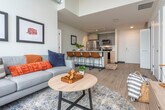 Located in Madison, WI, this modern 3-bedroom, 2-bathroom unit showcases an impressive open-concept design defined by soaring concrete ceilings and dramatic floor-to-ceiling windows that flood the interior with natural light. The combined kitchen and living area serves as the heart of the home, where the living room's expansive glazed walls frame sweeping views of the Madison skyline and the lake beyond. The kitchen is outfitted with stainless steel appliances, gray cabinetry, light wood flooring, and a generous white quartz island with bar seating — ideal for both cooking and casual dining. The living space flows seamlessly from the kitchen, offering an airy, loft-like ambiance accentuated by exposed ductwork and concrete architectural elements. The spacious primary bedroom continues the floor-to-ceiling window theme, offering stunning elevated city and water views, while the additional bedrooms are bright and well-proportioned with clean, minimal finishes. Both bathrooms feature crisp white quartz countertops, undermount sinks, large frameless mirrors, and glass-enclosed showers, delivering a sleek, contemporary aesthetic throughout. The overall palette of whites, light woods, and concrete creates a cohesive, modern atmosphere well-suited to urban living in the heart of Madison.
