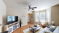 This single-story home in Conroe, TX (77304) offers a well-designed, open layout with warm neutral tones and wood-look flooring throughout the main living areas. The spacious living room features elevated ceilings, a ceiling fan, and multiple windows with white blinds that allow abundant natural light. An arched passageway adds an architectural accent, while a pass-through counter connects the living space to the kitchen area.

The kitchen is well-appointed with rich wood cabinetry, granite-style countertops, black appliances including a range and built-in microwave, a double stainless steel sink, and ample storage space extending to the upper walls. Adjacent to the kitchen, the dining area accommodates a full dining set and benefits from natural light through large windows.

The primary bedroom is generously sized with plush carpeting and a ceiling fan, and includes an en-suite bathroom with a granite-topped vanity, tile flooring, and a walk-in closet with built-in wire shelving. A second bedroom offers comfortable proportions, carpeted floors, and a window with natural light. The dedicated laundry room houses a full-size washer and dryer with overhead shelving and an electrical panel access point, adding practical utility to the home.