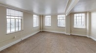 This single-floor unit is designed with a practical and straightforward layout. The living area is generously sized, featuring neutral beige walls, plush wall-to-wall carpeting, and elegant crown molding that adds a classic touch to the space. Multiple windows fitted with blinds allow natural light to fill the room, creating a bright and open atmosphere. An open doorway connects the living space to additional rooms, enhancing the sense of flow throughout the unit.

The bedroom offers ample space with the same carpeted flooring and crown molding details. Multiple windows provide good natural light, and a built-in closet with a hanging rod offers convenient storage.

The kitchen follows a U-shaped configuration, outfitted with white cabinetry, dark countertops, a coil-burner electric range, and a sink positioned beneath a window. Cork-style flooring ties the functional workspace together, and overhead ventilation is included above the stove.

The bathroom features a long, narrow layout with a white vanity, single sink, and generous counter space beneath a well-lit mirror. Light-toned flooring and white walls keep the space clean and functional. A frosted window at the far end of the bathroom provides additional natural light and ventilation.