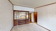Located at 49330 Carlos Street in Chesterfield, Michigan, this single-story, one-bedroom, one-bathroom home offers a practical and efficiently organized layout across its modest footprint. The living room serves as the central gathering space, finished with wall-to-wall carpeting, textured wallpaper, and wood crown molding throughout. A large front window allows natural light to pour in, offering a view of the surrounding neighborhood. The kitchen is separated from the living area by a distinctive wood-framed open divider featuring built-in shelving and storage cabinets below, creating a semi-open feel while defining each space. The kitchen itself includes upper cabinetry, a countertop with sink, and room for appliances. The bedroom is a comfortable, carpeted room with its own window fitted with vertical blinds, providing natural light and privacy. It connects conveniently to the rest of the home via a central hallway. The full bathroom features a tub and shower combination with chrome fixtures, a vanity with storage, and wood-look vinyl flooring. A dedicated utility room completes the home's functional layout. Textured ceilings and consistent wood-tone trim details are carried throughout, giving the home a cohesive, classic character.