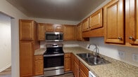This single-story unit in Louisville, KY offers a thoughtfully designed layout with distinct living, kitchen, and bedroom areas. The kitchen serves as a functional centerpiece, featuring warm honey-toned cabinetry extending from floor to ceiling, granite-style countertops, a stainless steel electric range, over-the-range microwave, double-basin sink with a modern pull-down faucet, and a dishwasher. Ample upper and lower cabinet storage makes the space highly practical.

The living area is generously proportioned, finished with durable hardwood-style plank flooring and neutral walls that create a bright, open atmosphere. A sliding glass door fills the space with natural light while providing direct views of the surrounding outdoor greenery. The layout reveals a separate dining or secondary living space adjacent to the kitchen, connected by an open passage.

Bedrooms are carpeted for comfort, with one featuring multiple windows that bring in abundant natural light and another equipped with a closet with rod and shelf storage. The bathroom includes a full tub-shower combination, a wood-vanity with integrated sink, a large mirror, and hardwood-style flooring, completing this well-appointed unit.