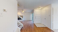 This two-story home offers a functional and well-organized layout across two floors. The main level features a welcoming entryway with tile flooring that transitions into warm hardwood-style flooring throughout the living and dining areas. The living room is highlighted by a ceiling fan, a classic brick fireplace, and sliding glass doors that bring in natural light. A breakfast bar connects the living area to the kitchen, which is outfitted with white cabinetry, tile flooring, and a full suite of white appliances including a refrigerator, electric range, and over-the-range microwave. A pendant light fixture illuminates the adjacent dining area, which also features hardwood-style flooring.

The upper floor houses all three bedrooms, each fitted with plush carpeting and ceiling fans. The primary bedroom offers a comfortable footprint, while the additional bedrooms include windows with views of surrounding greenery. The three bathrooms are finished with light tile flooring, white vanity cabinetry, and framed mirrors. A dedicated closet provides additional storage. Textured ceilings are consistent throughout the home, contributing to its classic character. Two staircases with carpeted treads connect the floors, enhancing circulation throughout the residence.